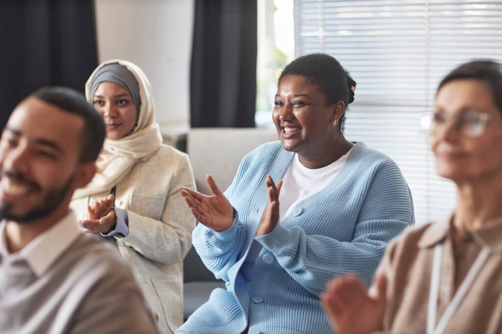 Young cheerful female student clapping her hands after report of speaker